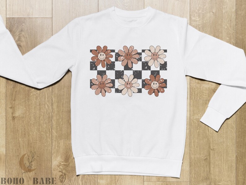 May include: White sweatshirt with a checkered pattern and brown flowers with smiley faces.