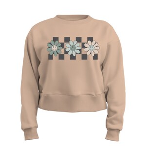 May include: A beige cropped sweatshirt with a black and white checkered pattern and three pastel green and blue flowers with smiley faces.