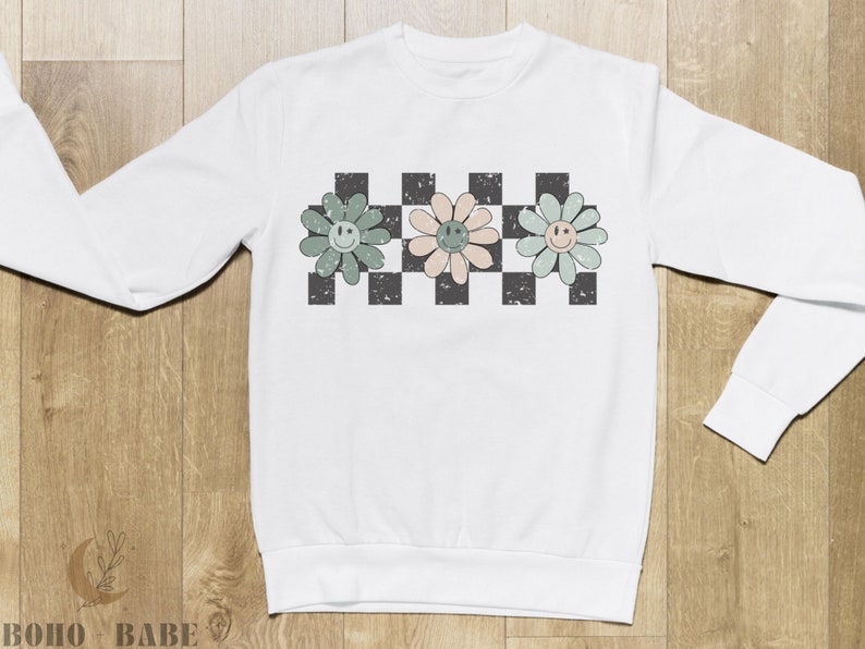May include: White long-sleeved sweatshirt with a checkered pattern and three smiling flower designs in green, pink, and blue.