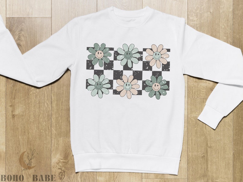 May include: White sweatshirt with a checkered pattern and green, pink, and blue flowers with smiley faces.