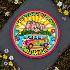 May include: A colorful round sticker featuring a retro-style VW bus with a peace sign and flower accents. The sticker reads "Devil's Lake State Park Wisconsin" in a psychedelic font, with a mountain and lake backdrop.