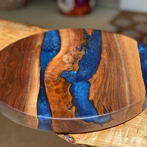 May include: Round wooden serving tray with a blue epoxy resin inlay. The wood has a rich brown color and the resin has a deep blue color with a slight sparkle.