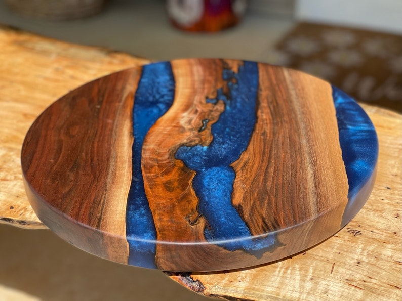 May include: Round wooden serving tray with a blue epoxy resin inlay. The wood has a rich brown color and the resin has a deep blue color with a slight sparkle.