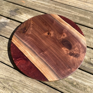 May include: A round wooden serving tray with a dark brown walnut wood top and a red epoxy resin edge.