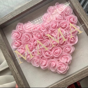 May include: A framed heart-shaped arrangement of pink artificial flowers with the word "MAMA" and the text "remarkable" in gold glitter lettering.