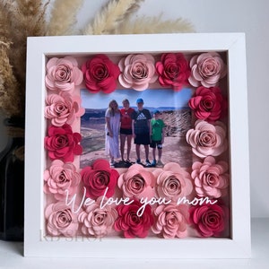 May include: White picture frame with a photo of a family of five standing in front of a desert landscape. The frame is decorated with pink and red paper flowers and the text "We love you mom" is written in white.