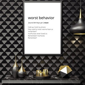 Può includere: Una stampa incorniciata in bianco e nero con il testo "worst behavior" e una definizione della parola. La stampa è appesa a una parete nera con un motivo geometrico. Ci sono tre oggetti decorativi su un tavolo nero davanti alla stampa.