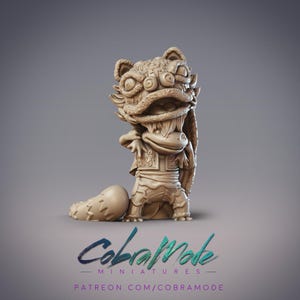 May include: A tan-colored miniature figurine of a lion dance character. The figure has a detailed lion head with large eyes and a wide mouth. The character is wearing a detailed costume. The text "CobraMode Miniatures" and a Patreon link are at the bottom.