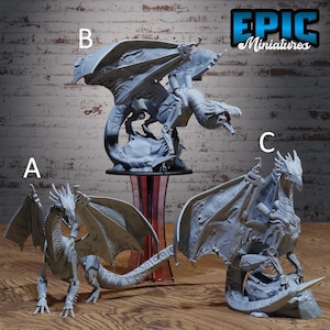 May include: Three grey dragon figurines with detailed wings and scales are displayed. The dragons are in various poses, with one standing, one perched, and one in flight. The Epic Miniatures logo is visible in the top right corner.