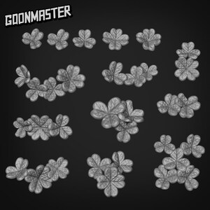 Puede incluir: Colección de objetos grises con forma de trébol de tres hojas sobre un fondo oscuro. El texto "GOONMASTER" se muestra en la esquina superior izquierda. Los tréboles están en varias disposiciones, algunos agrupados y otros en filas.