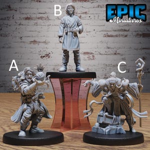 May include: Three unpainted gray resin tabletop gaming miniatures labeled A, B, and C. Figure A is a standing spellcaster with flowing robes. Figure B is a standing character in a tunic on a pedestal. Figure C is a crouching figure holding a staff.