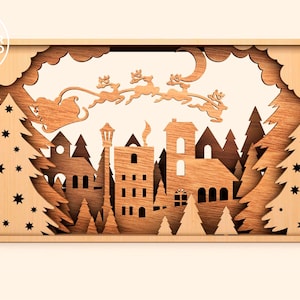 May include: A wooden Christmas scene with a cutout of Santa Claus flying in a sleigh pulled by reindeer over a town with houses and trees. The scene is framed in wood and has a white background.