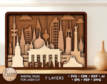 May include: A laser cut wooden model of the Berlin skyline, featuring iconic landmarks like the Brandenburg Gate and the Reichstag Building. The model is made of multiple layers of wood and is designed to be assembled. The text "GERMANY" is displayed at the bottom of the model.