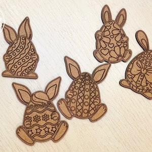 May include: Five wooden Easter bunny cutouts with different patterned eggs. The bunnies are holding the eggs in their front paws. The eggs are decorated with hearts, stripes, polka dots, and flowers.