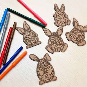 May include: Five unfinished wooden Easter bunny ornaments with intricate designs. The bunnies are shaped like eggs and have different patterns. A set of colorful markers are also included.