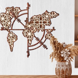 May include: A wooden world map wall decor with a compass design. The map is made of laser-cut wood and has a light brown finish. The compass is made of dark brown wood and has a white background. The map is mounted on a white wall.