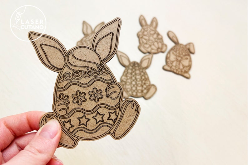 May include: Five wooden Easter bunny ornaments, each shaped like a bunny holding an egg. The eggs are decorated with different patterns, including swirls, stars, and flowers. The ornaments are a light brown color.