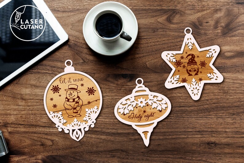 Puede incluir: Tres adornos navide&ntilde;os de madera blanca con dise&ntilde;os intrincados. Un adorno presenta un mu&ntilde;eco de nieve con el texto "let it snow", otro tiene el texto "Holy night", y el tercero es una estrella con un mu&ntilde;eco de nieve dentro.
