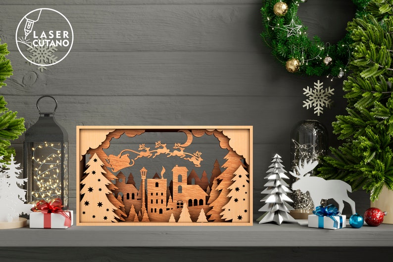 May include: A wooden Christmas scene with a cutout of Santa Claus flying in a sleigh pulled by reindeer over a town with trees and stars. The scene is illuminated with lights and is surrounded by other Christmas decorations.