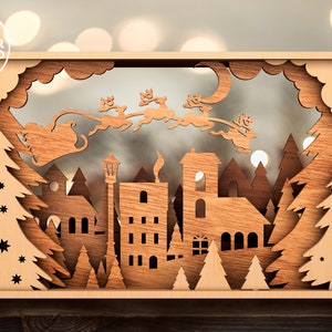 May include: A wooden Christmas scene with Santa Claus flying over a town with a church, houses, and trees. The scene is cut out of wood and has a 3D effect.