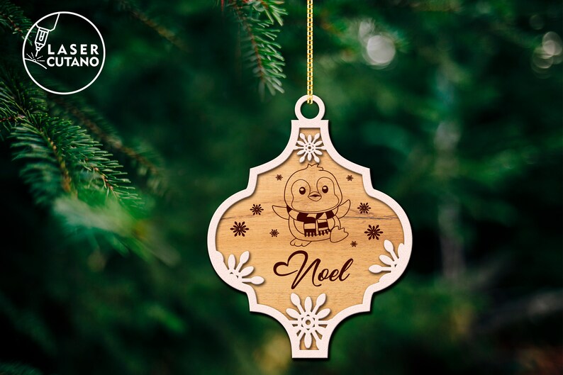 Puede incluir: Un adorno navide&ntilde;o de madera con un contorno blanco y un ping&uuml;ino con una bufanda. El adorno dice "No&euml;l" en el centro.