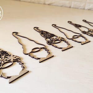 Pu&ograve; includere: Sette ornamenti di gnomo in legno con intricati disegni floreali. Gli gnomi sono tutti rivolti nella stessa direzione e hanno un design semplice e minimalista.