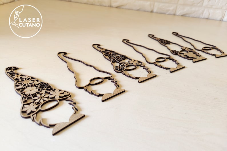 Pu&ograve; includere: Sette ornamenti di gnomo in legno con intricati disegni floreali. Gli gnomi sono tutti rivolti nella stessa direzione e hanno un design semplice e minimalista.