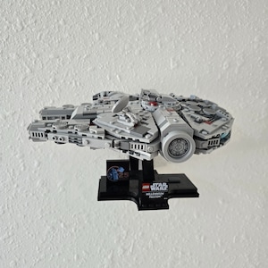 Peut inclure: Un modèle Lego du Faucon Millenium gris avec des accents rouges et bleus. Le modèle est sur un socle noir avec un logo Lego Star Wars 25e anniversaire et les mots "Millennium Falcon".
