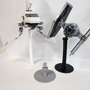 May include: Two Star Wars Lego spaceship models on display stands. The white spaceship is on a white stand and the black spaceship is on a black stand.