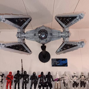 May include: A grey TIE Silencer Star Wars spaceship model with black details hangs from the ceiling. A group of Star Wars action figures stand in a row below the spaceship.