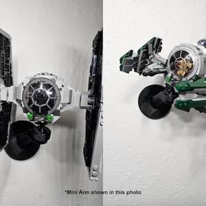 May include: A black plastic mini arm mount attached to a wall, supporting a gray and black TIE fighter model on the left and a green, gray, and white starfighter model with a small droid figure on the right. The text *Mini Arm shown in this photo is visible.