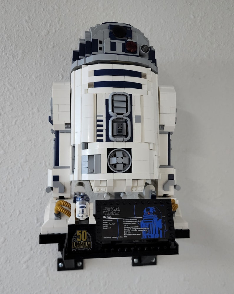 May include: A white and blue LEGO Star Wars R2-D2 model with a black display stand. The stand features a small LEGO R2-D2 figure and a black plaque with the text "STAR WARS R2-D2" and technical specifications. The stand also has a 50th anniversary Lucasfilm logo.