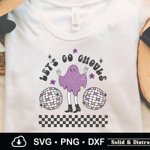 May include: A white t-shirt with a purple ghost wearing a black and white checkered pattern. The ghost is holding a disco ball and the text "Let's Go Ghouls" is written in a retro font.