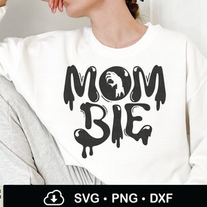 May include: White sweatshirt with black text that reads "Mom-bie" with a dripping effect. The "o" in "Mom" is replaced with a black circle with a white hand reaching out from inside.