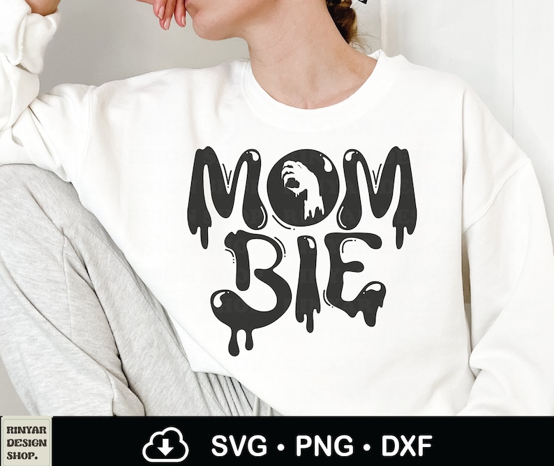 May include: White sweatshirt with black text that reads "Mom-bie" with a dripping effect. The "o" in "Mom" is replaced with a black circle with a white hand reaching out from inside.