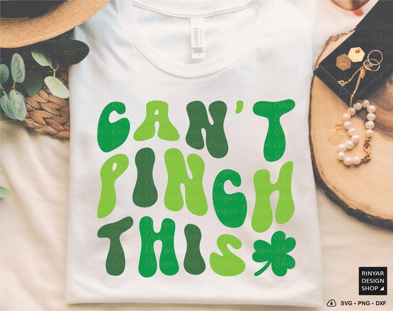 Peut inclure: Un t-shirt blanc avec un graphique vert qui dit "Can't Pinch This" dans une police r&eacute;tro. Une tr&egrave;fle vert se trouve &agrave; droite du texte.