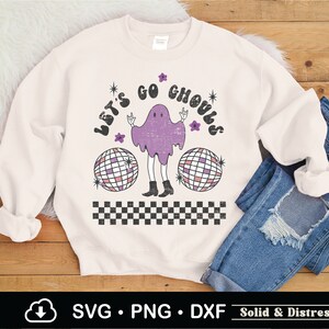May include: A white sweatshirt with a distressed graphic design featuring a purple ghost with a disco ball and the text "Let's Go Ghouls".