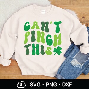 Peut inclure: Un sweat-shirt blanc avec le texte "Can't Pinch This" en lettres ondul&eacute;es vertes. Une tr&egrave;fle vert se trouve &agrave; droite du texte.