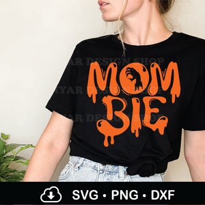 May include: Black t-shirt with orange text that reads "Mom Bie" with a zombie hand in a circle above the word "Mom".