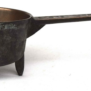 May include: A small, three-legged bronze pot with a long handle. The pot has a dark brown patina and is likely antique.