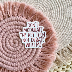 May include: White sticker with red text that reads "Don't modulate the key then not debate with me". The sticker is on a pink and white woven rug.