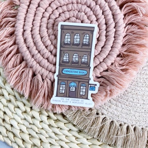 Pode incluir: Um adesivo de um prédio marrom com uma marquise azul e o texto "Cornerstone Books" acima da porta. O adesivo também inclui o texto "On the corner of Diagon Alley & Horizont Alley".