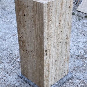 Puede incluir: Un gran pedestal cuadrado de travertino beige con un patr&oacute;n veteado marr&oacute;n claro. El pedestal est&aacute; sentado sobre una base cuadrada gris.
