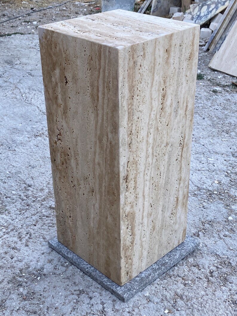 Puede incluir: Un gran pedestal cuadrado de travertino beige con un patr&oacute;n veteado marr&oacute;n claro. El pedestal est&aacute; sentado sobre una base cuadrada gris.