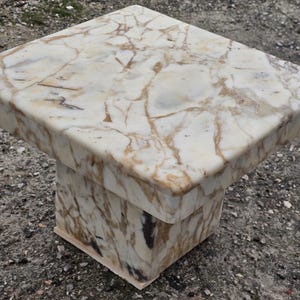 May include: A square side table constructed from polished stone with a cream and white base color featuring prominent brown and tan veining throughout the surface. The table has a thick, flat top and a sturdy, block-shaped pedestal base.