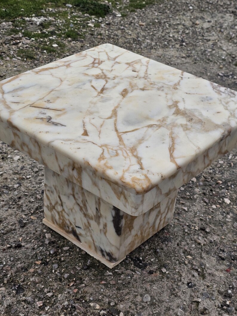 May include: A square side table constructed from polished stone with a cream and white base color featuring prominent brown and tan veining throughout the surface. The table has a thick, flat top and a sturdy, block-shaped pedestal base.