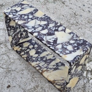 May include: A rectangular marble object with a hollow center. The marble has a pattern of white, cream, and dark purple veining. The object is sitting on a gray concrete surface.
