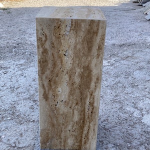 Puede incluir: Un gran bloque rectangular de travertino con un patr&oacute;n veteado natural en tonos beige, marr&oacute;n y crema. La piedra est&aacute; sobre una superficie gris.