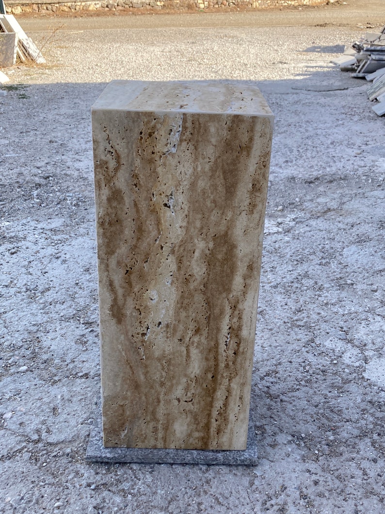 Puede incluir: Un gran bloque rectangular de travertino con un patr&oacute;n veteado natural en tonos beige, marr&oacute;n y crema. La piedra est&aacute; sobre una superficie gris.