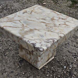 May include: A square side table constructed from white marble with prominent brown and grey veining. The table features a thick, flat top surface supported by a central, block-style pedestal base that matches the marble pattern of the top.